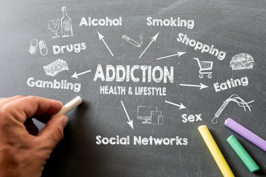 A man listing addictions influencing health and lifestyle on a blackboard.