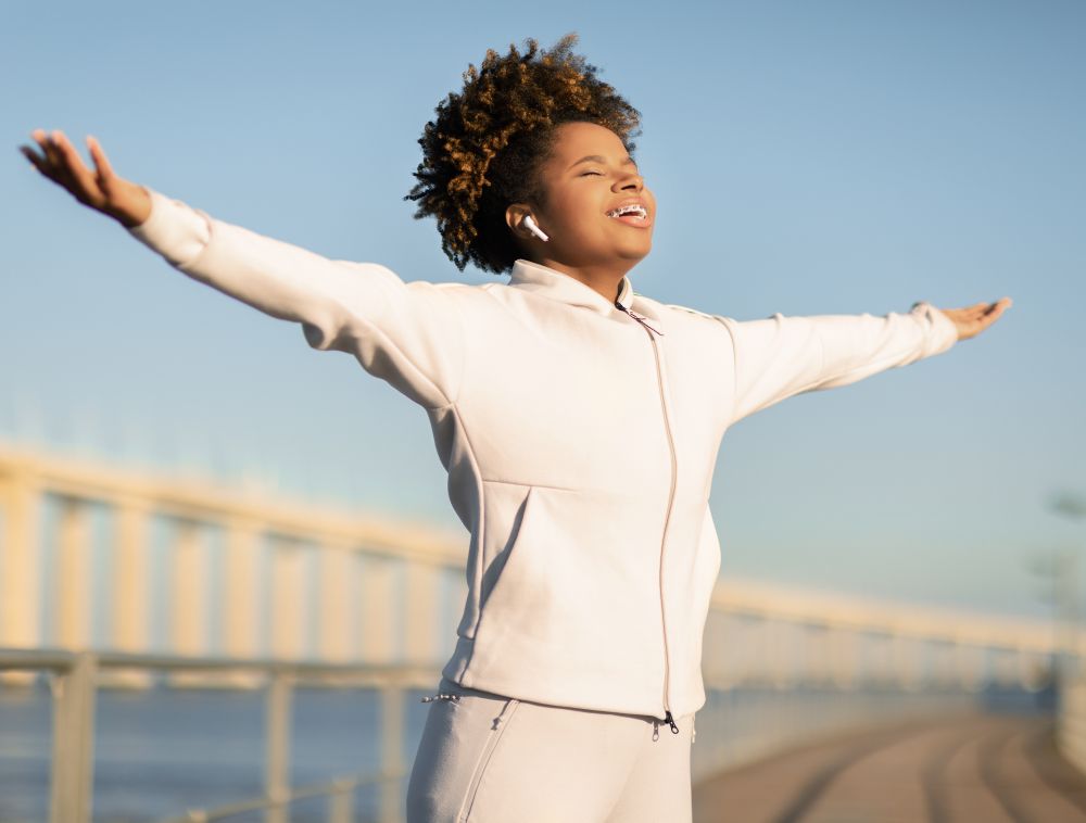 Young Afro-American jogger woman breathing deeply standing with her arms stretched.