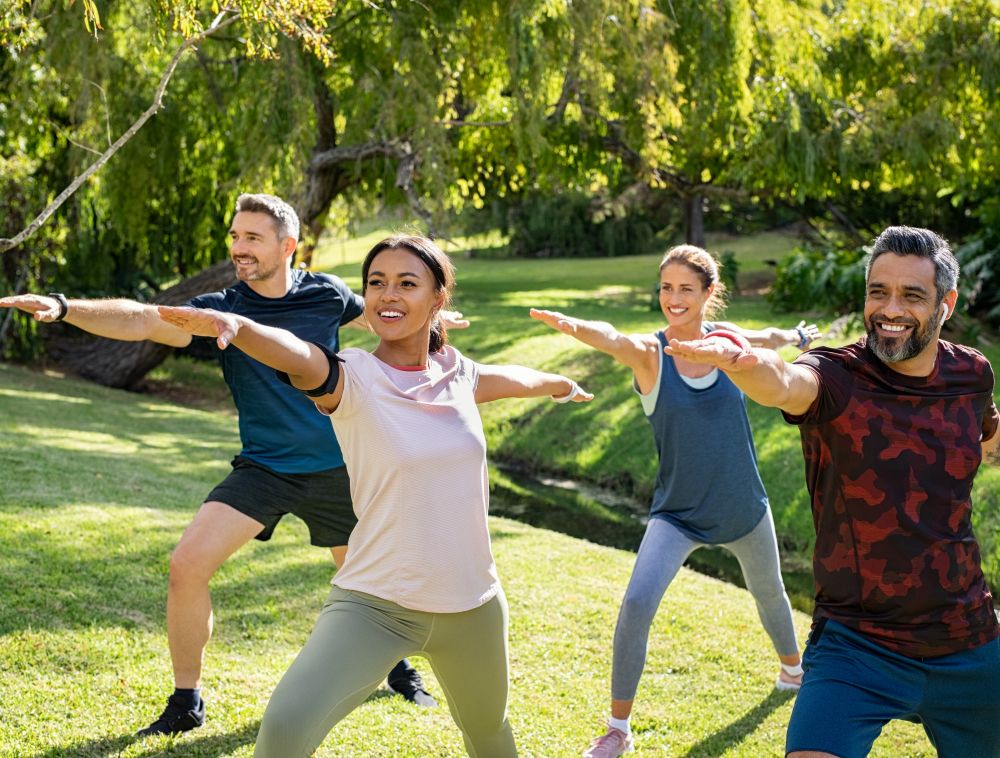 Mature multiethnic couple doing sport and physical exercises out Group of cheerful women and men practicing yoga outdoors.