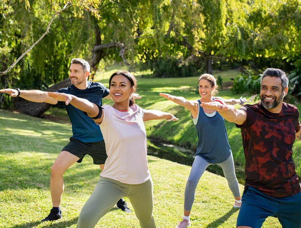 Group of cheerful women and men practicing yoga outdoors.