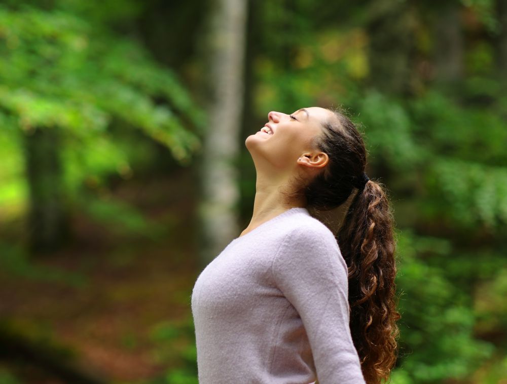 Happy woman breathing air deeply while enjoying a walk in a forest.