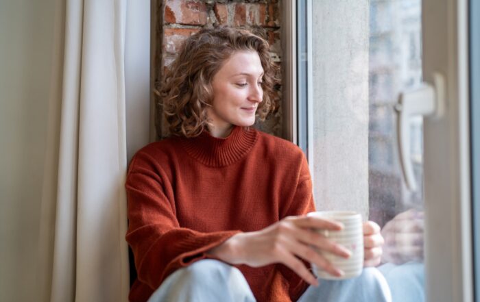 Calm satisfied woman freelancer taking pause from remote work for stress free at home. Relaxed dreamy young female enjoying mindful break on windowsill holding warm cup of coffee. Burnout relieve.